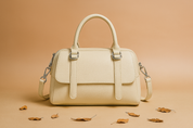 Off-white structured leather satchel handbag with silver hardware, top handles, and shoulder strap, displayed on a warm-toned studio platform