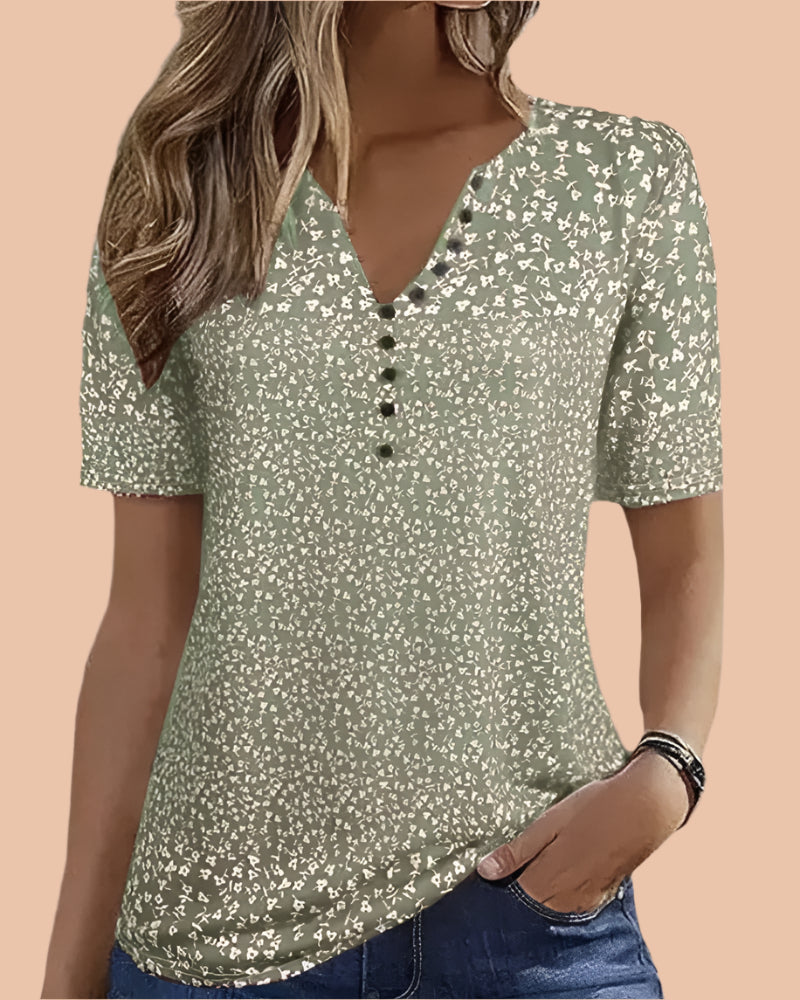 Olive green short-sleeve blouse with a scattered white floral print, V-neckline, and decorative black buttons; casual yet feminine top designed with a soft, lightweight fabric and a flattering hip-length cut.