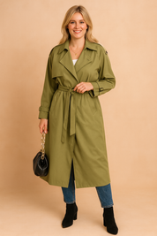 Olive-green belted trench coat with wide lapels, button details, and adjustable cuffs, styled with blue jeans, black ankle boots, and a black handbag.