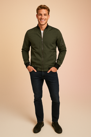 Olive green bomber jacket with front zipper, ribbed cuffs and hem, and zippered sleeve pocket, paired with dark slim-fit jeans and black low-top sneakers