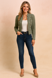 Olive-green military-style cropped jacket with front button detailing, paired with a white scoop-neck tank top, dark blue skinny jeans, black belt with gold buckle, and taupe pointed-toe heels.