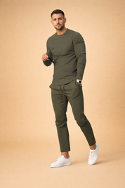 Olive green slim fit long sleeve crewneck shirt paired with matching tapered jogger pants featuring a smooth stretch fabric, clean seam detailing, adjustable drawstring waist, and white minimalist low-top sneakers for a modern athleisure look.