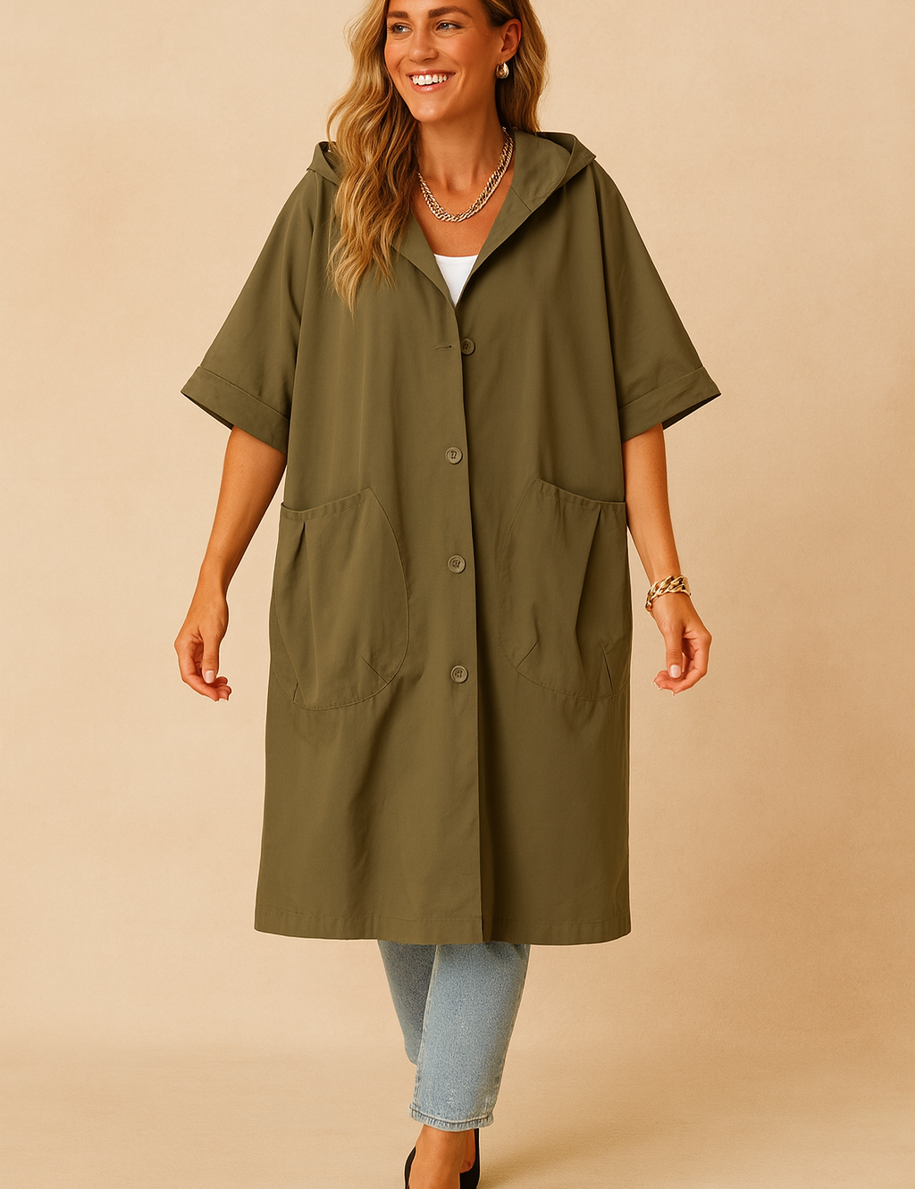 Olive green oversized hooded coat with short sleeves, four front buttons, and two large front patch pockets, styled over light blue jeans and paired with black pointed heels.