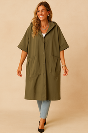 Olive green oversized hooded coat with short sleeves, four front buttons, and two large front patch pockets, styled over light blue jeans and paired with black pointed heels.