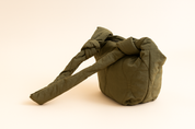  Olive-green quilted handbag with knotted padded handles and a soft cube shape, displayed against a neutral gradient background.