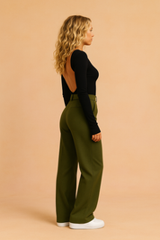 Olive green wide-leg tailored trousers with a high waist and minimal pleat structure, styled with a black open-back fitted long-sleeve top and white sneakers.