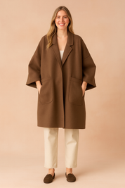 Oversized brown wool coat with wide sleeves, large front pockets, and relaxed fit, styled over light trousers and loafers for a minimalist chic look.