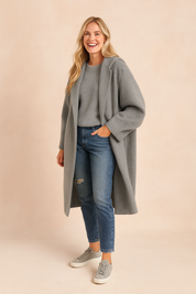 Oversized grey long wool coat with relaxed sleeves, styled with a light grey ribbed sweater, distressed blue jeans, and grey low-top sneakers.