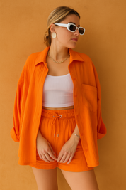 Oversized orange co-ord set featuring a long-sleeve button-up shirt and drawstring shorts with a textured finish, paired with a white ribbed bandeau top for a bold yet casual summer look.