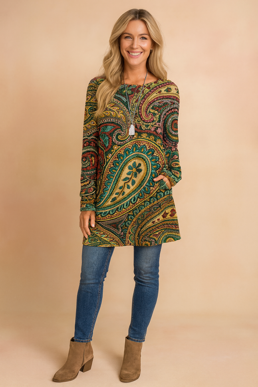 Long-sleeve tunic with intricate paisley print in green, gold, red, and teal tones, paired with slim blue jeans and tan ankle boots.