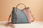 Two-toned structured handbag in pastel blue and soft pink faux leather with white stitching, gold hardware, heart-shaped charm with pearl and tassel, and detachable shoulder strap.