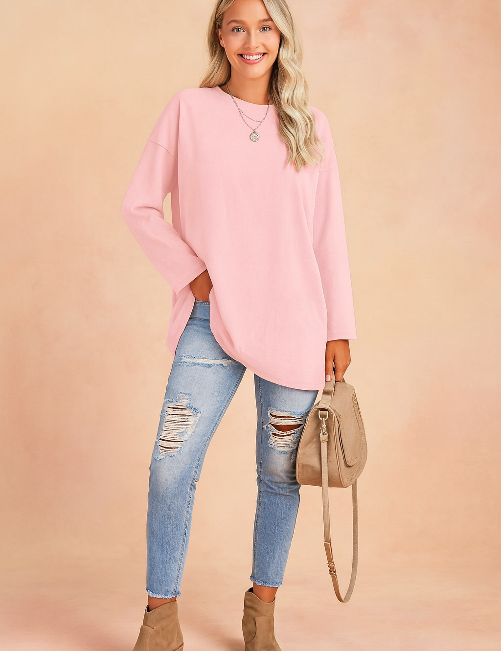 Pastel pink oversized long-sleeve tunic paired with light-wash distressed skinny jeans, taupe suede ankle boots, and a matching beige crossbody handbag.