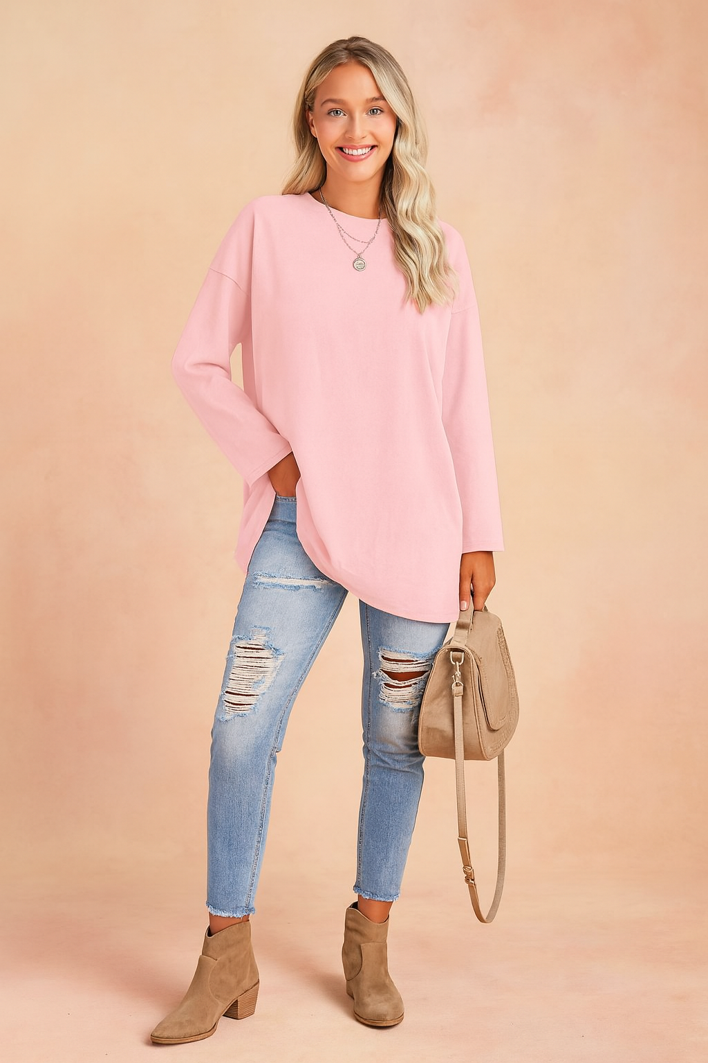 Pastel pink oversized long-sleeve tunic paired with light-wash distressed skinny jeans, taupe suede ankle boots, and a matching beige crossbody handbag.