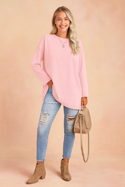 Pastel pink oversized long-sleeve tunic paired with light-wash distressed skinny jeans, taupe suede ankle boots, and a matching beige crossbody handbag.