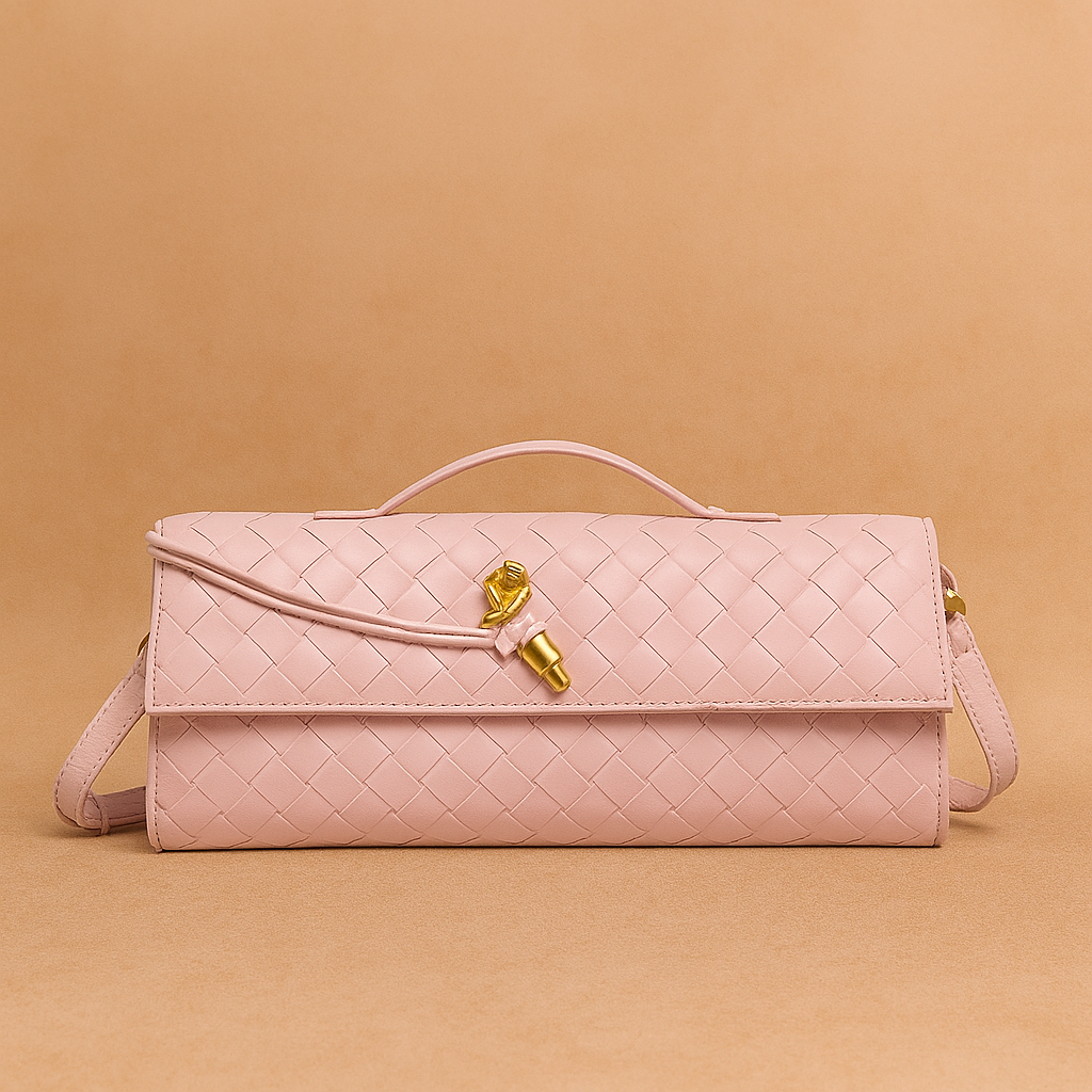 Pastel pink woven leather handbag with top handle, gold-tone hardware, and slim rectangular silhouette, placed on a warm sand and blush-toned gradient background.