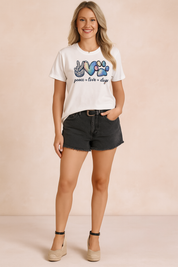 White short-sleeve graphic tee featuring a colorful peace sign, heart, and paw print motif with the text "peace ♥ love ♥ dogs," paired with high-waisted black frayed shorts and beige platform espadrilles.