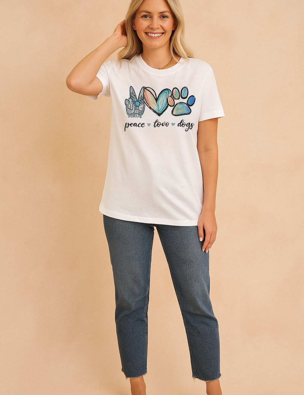White graphic T-shirt with colorful "peace love dogs" print featuring a peace hand sign, heart, and paw print, styled with blue jeans and white crossover sandals.