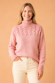 Soft pink cable-knit high-neck sweater with braided pattern across the upper bodice and ribbed cuffs, paired with cream straight-leg jeans.