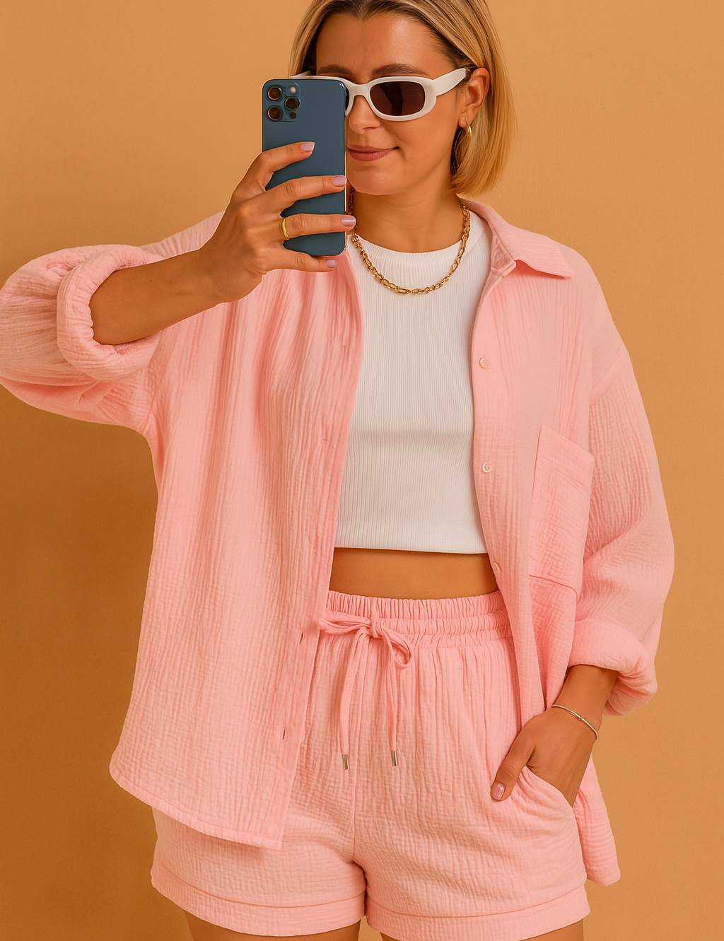 Casual crinkle-knit co-ord set with a long-sleeve button-up shirt and drawstring shorts in soft pastel pink, styled over a fitted white ribbed crop top.