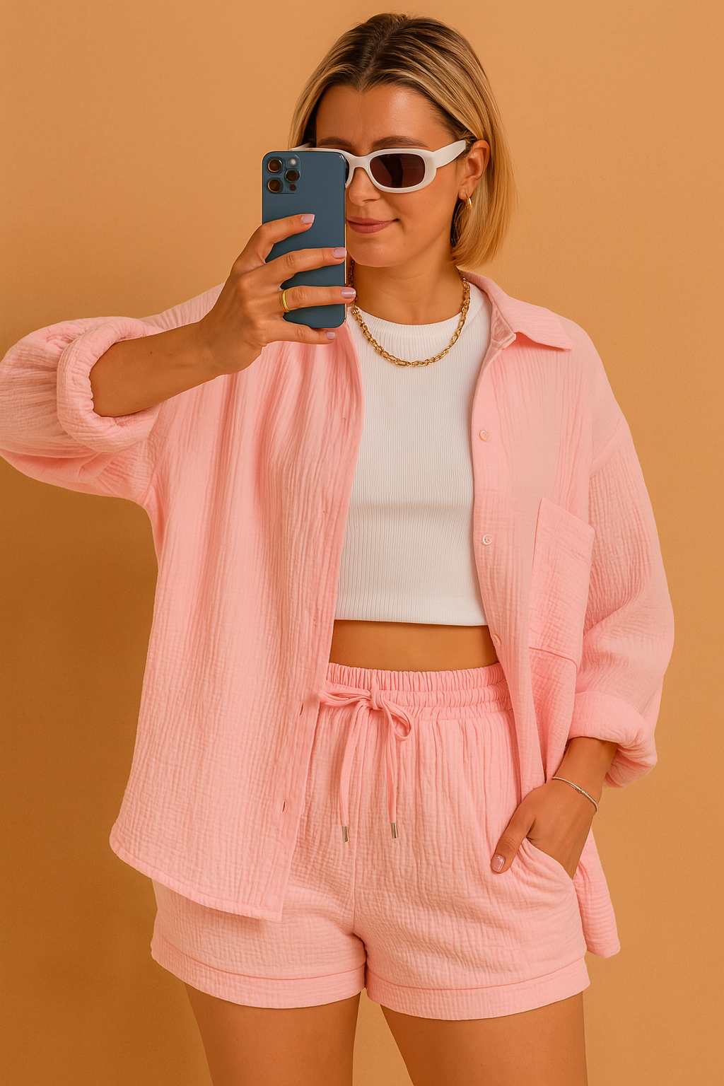 Casual crinkle-knit co-ord set with a long-sleeve button-up shirt and drawstring shorts in soft pastel pink, styled over a fitted white ribbed crop top.
