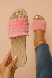 Pink fringe-textured slide sandals with a ridged sole and layered fabric bands, designed for casual summer wear.