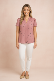 Soft pink V-neck blouse with short puff sleeves and a front pleat detail, adorned with evenly spaced small black heart prints, paired with slim-fit white trousers.