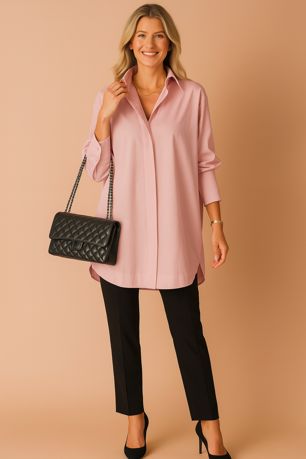 Elegant light pink oversized button-down tunic paired with slim black trousers and a quilted leather shoulder bag, styled with black heels and minimal gold jewelry for a polished look.