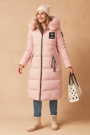 Pink long winter parka jacket with faux fur hood, quilted design, front zipper closure, side pockets, and decorative patches, styled with jeans and beige lace-up boots, paired with a white cutout tote bag
