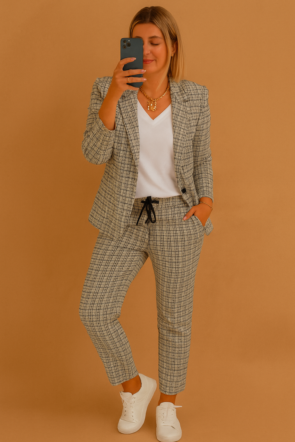 Plaid two-piece set featuring a tailored blazer and tapered drawstring pants in gray and black checkered pattern, styled with a white V-neck top and white sneakers.