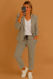Plaid two-piece set featuring a tailored blazer and tapered drawstring pants in gray and black checkered pattern, styled with a white V-neck top and white sneakers.