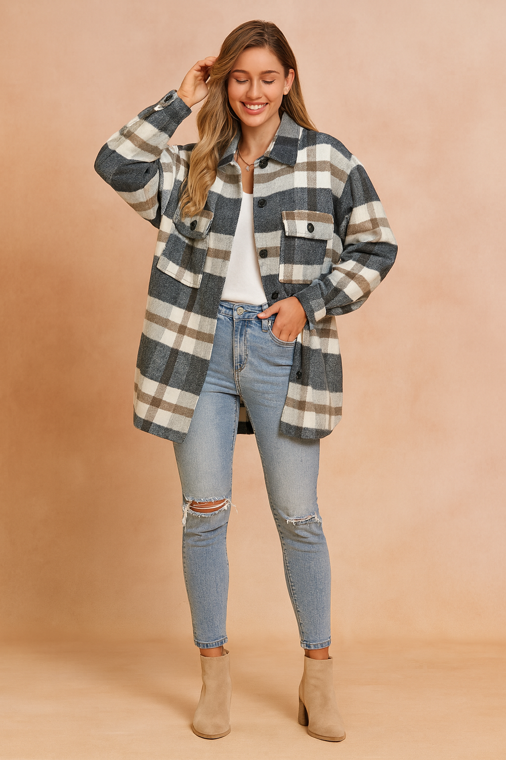 Oversized plaid shacket in grey, white, and brown check pattern, featuring front button closure, dual chest flap pockets with buttons, and a relaxed longline cut. Styled over a white top with distressed light-wash skinny jeans and beige ankle boots for a casual-chic layered look.