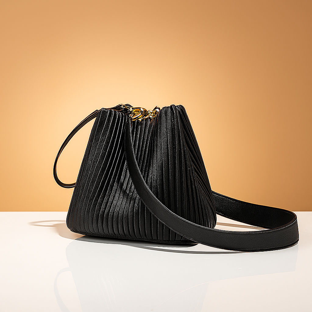 Pleated black leather handbag with gold hardware and long strap, showcased on a glossy surface with warm gradient background.