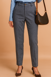 Tailored high-waisted grey herringbone trousers with a single front button, front pleats, belt loops, and tapered legs, styled with brown pointed-toe heels.