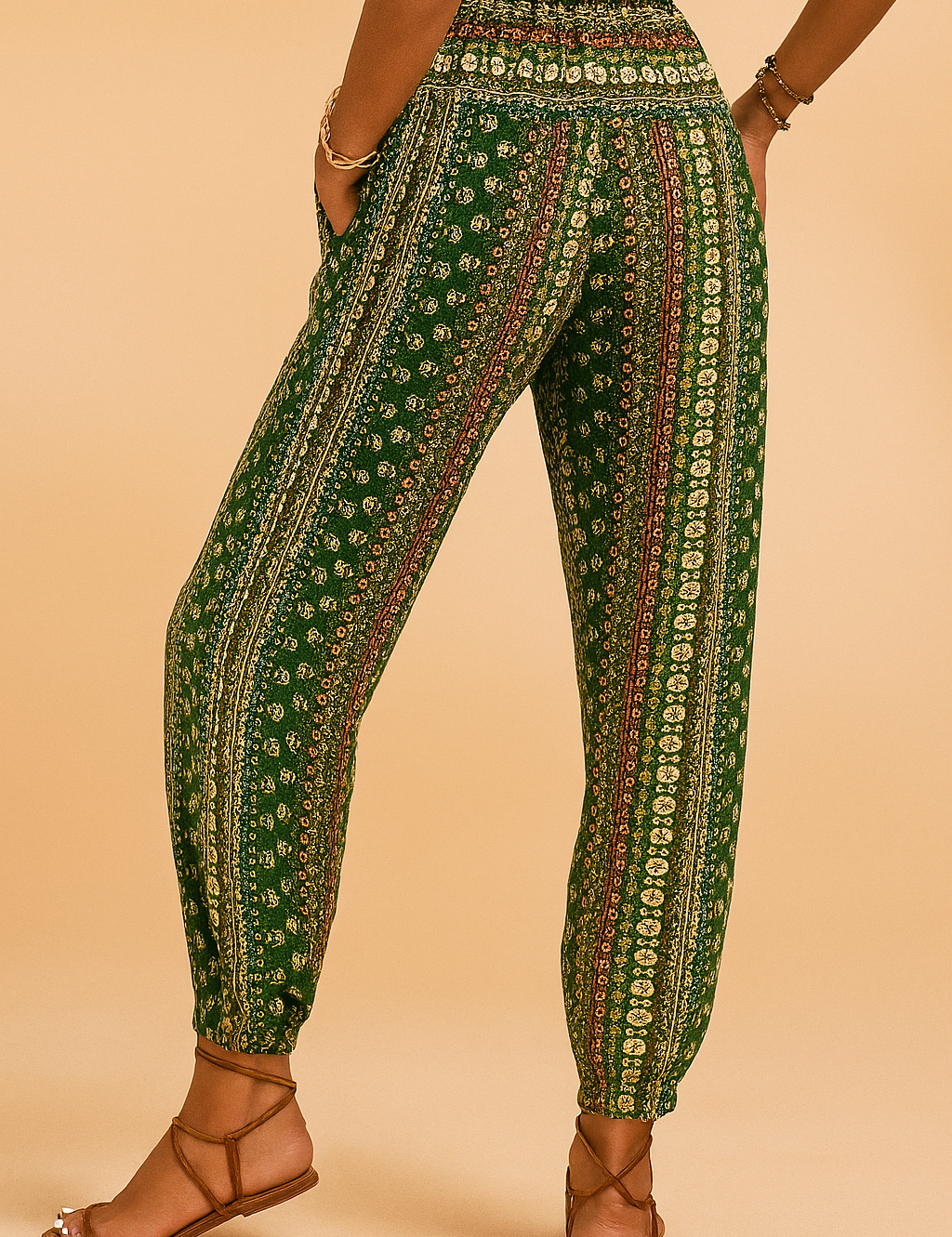 Bohemian green patterned jogger pants with a high elastic waistband and tapered ankle cuffs, featuring vertical floral and geometric stripes in cream and rust tones, paired with tan strappy sandals.