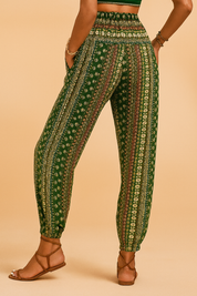 Bohemian green patterned jogger pants with a high elastic waistband and tapered ankle cuffs, featuring vertical floral and geometric stripes in cream and rust tones, paired with tan strappy sandals.