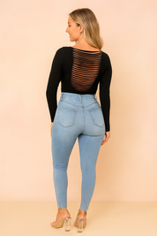 High-waisted light blue skinny jeans with subtle fading and stitched back pockets, paired with a black long-sleeve top featuring horizontal cutout detailing on the back, styled with transparent high-heel sandals