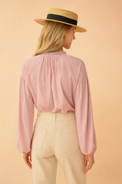 Pink and white pinstriped long-sleeve blouse with gathered neckline paired with high-waisted cream trousers, featuring back pockets and a clean tailored finish.