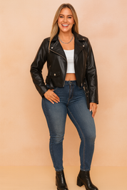 Black faux leather biker jacket with belted waist, silver zipper and button details, styled with slim-fit blue denim jeans and black ankle-strap heels.