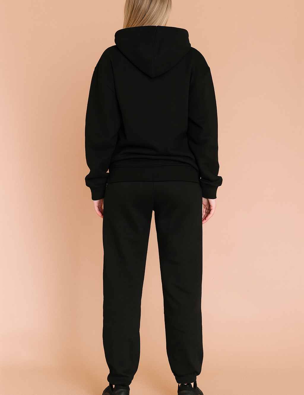 Black relaxed-fit hoodie and matching jogger sweatpants set, crafted from soft cotton fleece with ribbed cuffs and hem, styled with chunky black sneakers.