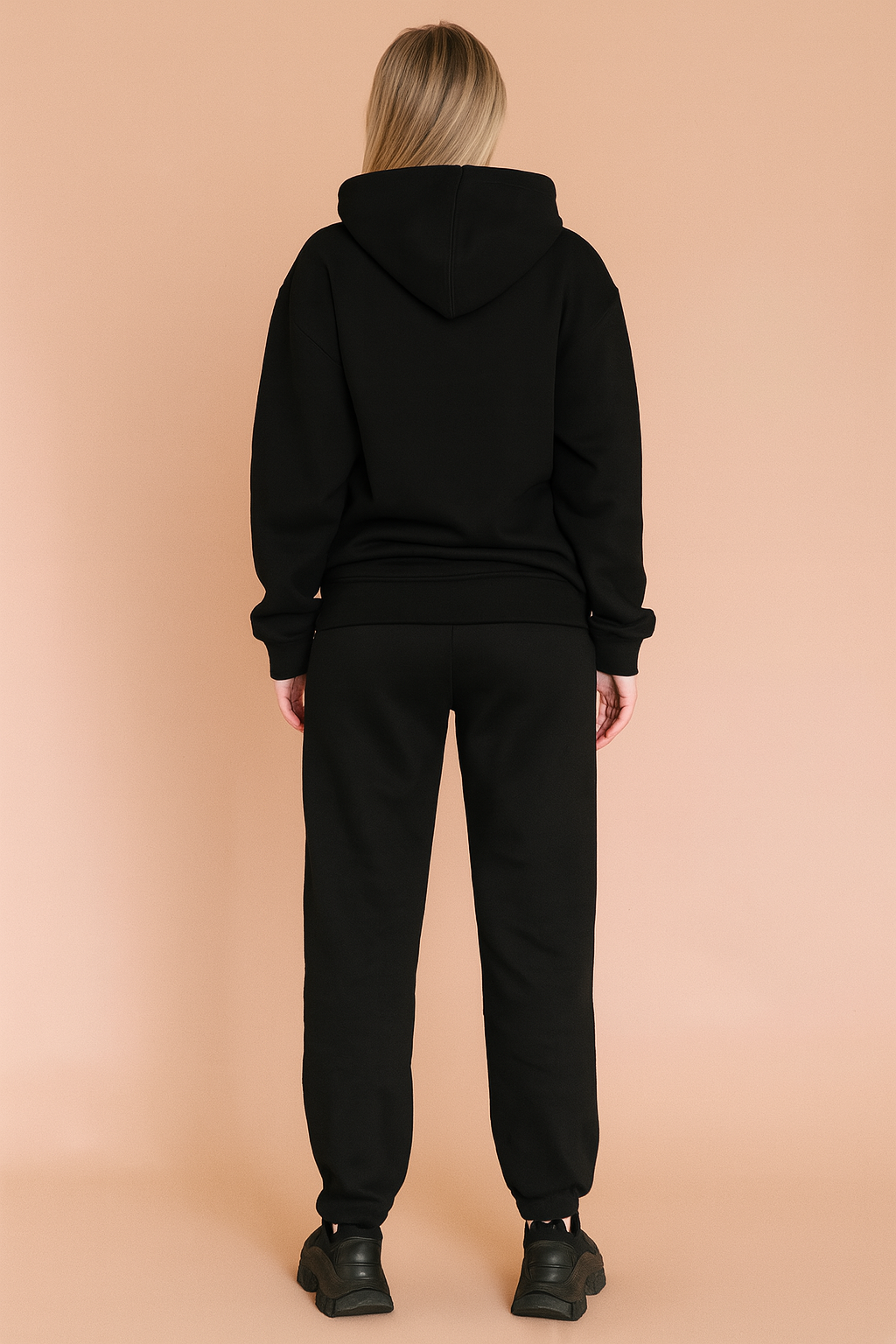 Black relaxed-fit hoodie and matching jogger sweatpants set, crafted from soft cotton fleece with ribbed cuffs and hem, styled with chunky black sneakers.