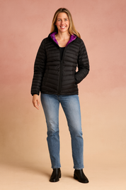  Black quilted puffer jacket with magenta interior lining, featuring a hood, front zipper closure, and two zippered side pockets, paired with light blue straight-leg jeans and black ankle boots.

