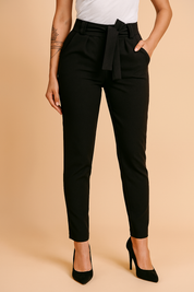 Tailored high-waisted black paperbag trousers with a matching fabric belt and tapered legs, styled with sleek black pointed-toe heels and a simple white tucked-in top.