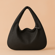 Black woven crescent hobo handbag with zipper closure, displayed on a warm beige backdrop with soft studio lighting.