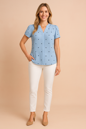 Light blue short-sleeve blouse with delicate puff shoulders, featuring evenly spaced small black heart patterns and a concealed front placket.