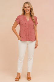 Dusty rose short-sleeve blouse with ruched shoulders and scattered small black heart print, featuring a V-neckline and hidden front placket design.