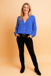 Blue geometric print long-sleeve blouse with a relaxed collar and deep neckline, paired with high-waisted black slim pants and a circular-buckle belt.