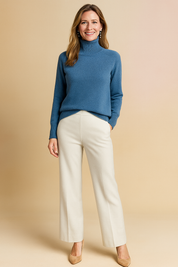 Soft knit blue turtleneck sweater with ribbed high neck and cuffs, paired with cream tailored wide-leg trousers and beige suede heels.