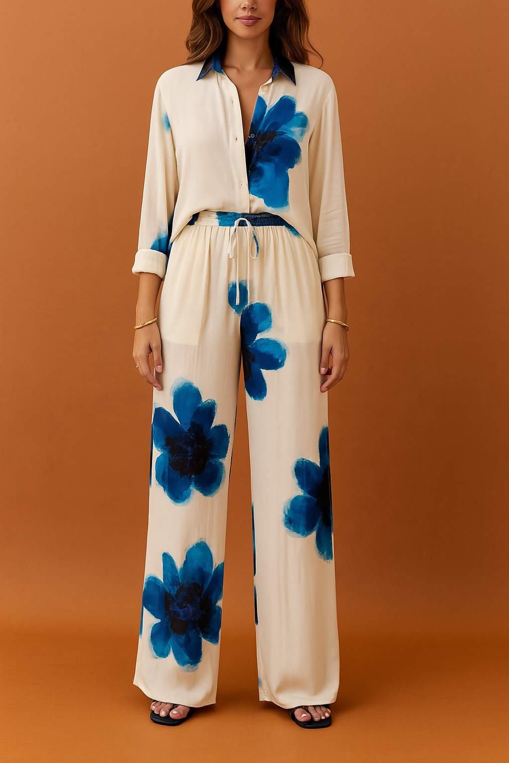 Cream two-piece coord set featuring a long-sleeve button-down shirt and wide-leg drawstring trousers, both adorned with oversized blue watercolor floral prints. Crafted from lightweight, fluid fabric with a soft drape and subtle sheen, offering a bold yet elegant daytime resort look.

