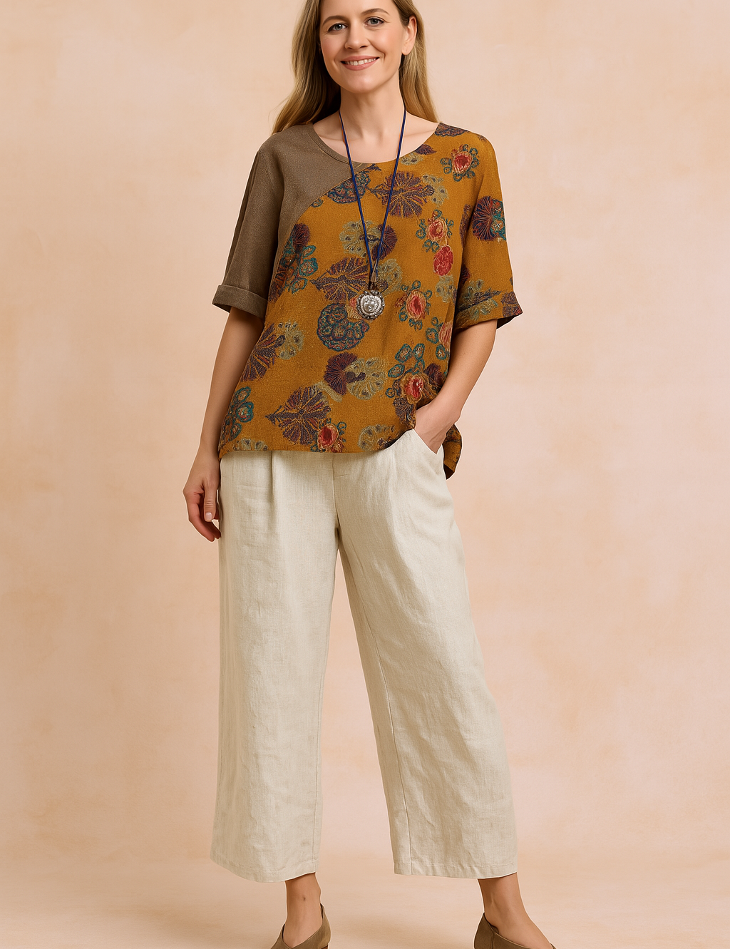 Loose-fit asymmetric blouse with rich amber-orange base, featuring colorful fan and floral prints in purple, blue, and red, button-accented at the shoulder and paired with neutral beige wide-leg trousers.