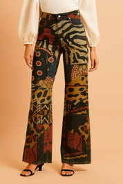 Bold patterned wide-leg pants with eclectic tribal and geometric motifs in mustard, rust, black, and navy, styled with a white blouse and black heeled sandals.